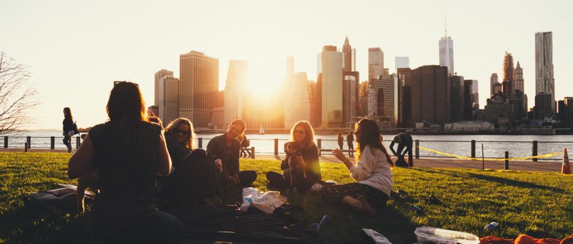 Friends sitting together on the grass at sunset, looking out over a city